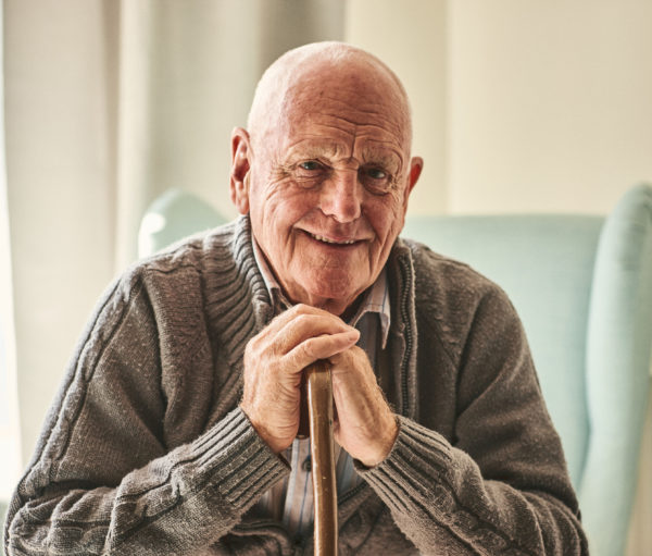 Happy elder man sitting on couch with a cane