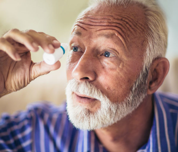 elder man putting drops into his eyes