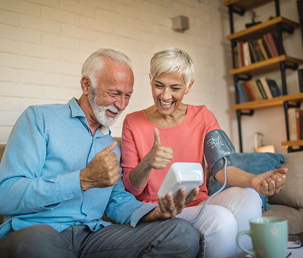 senior couple taking blood pressure and giving a thumbs up as they read the results